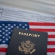 Blurred U.S. standard application certificate of live birth application form next to American flag and Passport of USA. Close up view.