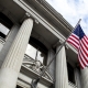 Stone granite official government building in city with American flag waving and flying in the wind, looking up, outside, judicial, freedom, civil courts, columns, criminal justice, law