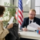 Portrait of male worker revising documents of young woman applying for visa in US immigration office