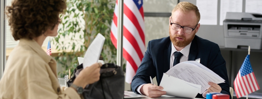 Portrait of male worker revising documents of young woman applying for visa in US immigration office